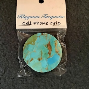 May include: A round cell phone grip with a Kingman turquoise design. The grip is packaged in a clear plastic bag with a white label that reads "Kingman Turquoise Cell Phone Grip".