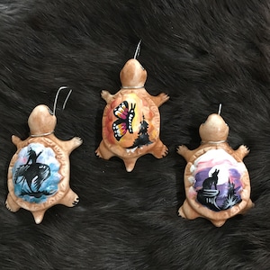 May include: Three hand-painted ceramic turtle ornaments. Each turtle features a different design: a butterfly, a Native American on horseback, and a wolf howling at the moon.