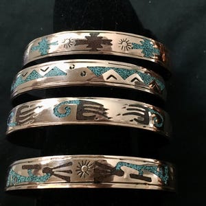 May include: Four silver-coloured cuff bracelets with turquoise inlay and etched Southwestern designs. Each bracelet features unique geometric and sunburst patterns, with dark brown accents. The bracelets are stacked, showcasing the intricate details.