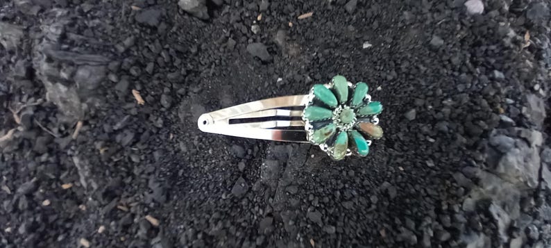 May include: A silver-toned metal hair clip featuring a decorative flower-shaped ornament. The ornament is composed of multiple teardrop-shaped turquoise stones arranged in a radial pattern around a small central stone, creating a floral design.