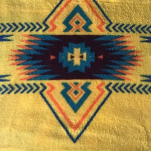 May include: A yellow blanket with a geometric pattern in shades of blue, teal, orange, and red. The pattern is a diamond shape with a smaller diamond in the center.