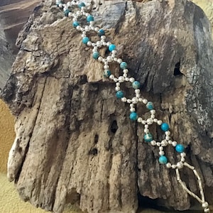 May include: A silver and turquoise beaded bracelet with a geometric pattern. The bracelet is made with small, round turquoise beads and silver spacer beads.
