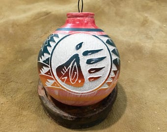 Peut inclure: Ornement décoratif rond peint à la main avec un motif tribal. L'ornement présente un dessus rouge, un centre blanc avec une figure stylisée et des accents orange et sarcelle. Il repose sur une petite base en bois ronde.