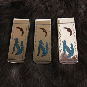 May include: Three silver money clips with turquoise and red inlay designs. Each clip features a stylised wolf howling at the moon.