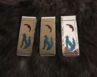 May include: Three silver money clips with turquoise and red inlay designs. Each clip features a stylized wolf howling at the moon.