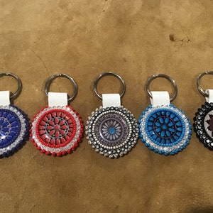 May include: Five beaded keychains with different colored and patterned designs. The keychains are attached to silver key rings and white leather straps.