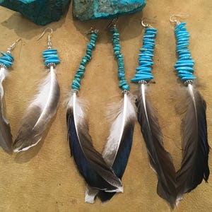 May include: Three pairs of dangle earrings featuring bright blue turquoise chip beads, silver-toned metal spacers, and long, natural-looking feathers with white, grey, and dark brown color gradients, suspended from silver-toned metal earring hooks.