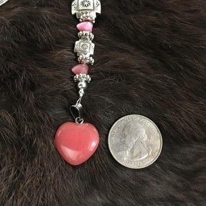 May include: A pink heart-shaped pendant with a silver chain and beads. The pendant is about the size of a quarter.