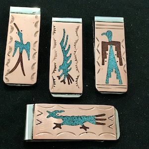 Può includere: Quattro fermasoldi in metallo con disegni del sud-ovest. Ogni fermasoldi presenta un diverso design intarsiato in turchese su uno sfondo color rame. Le clip hanno bordi color argento e raffigurano uccelli stilizzati e altre figure.