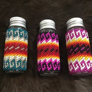 May include: Three small glass bottles with silver lids, each decorated with a colorful beaded pattern. The patterns feature geometric designs in shades of red, orange, yellow, white, black, pink, and blue.