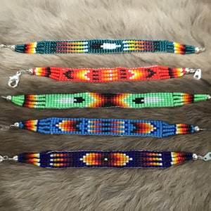 Op de afbeelding: Vijf kralenarmbanden met kleurrijke geometrische patronen. De armbanden zijn gemaakt van kleine, kleurrijke kralen en hebben zilveren sluitingen.