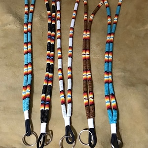 Peut inclure: Cinq lanières à perles avec des perles de différentes couleurs et un anneau de clé argenté à l'extrémité. Les lanières sont faites de perles noires, blanches, brunes, bleues et rouges.