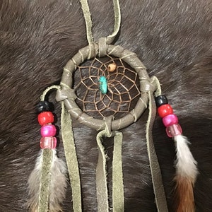 May include: A brown leather dreamcatcher with a turquoise stone, brown and orange beads, and white and brown feathers hanging from it.