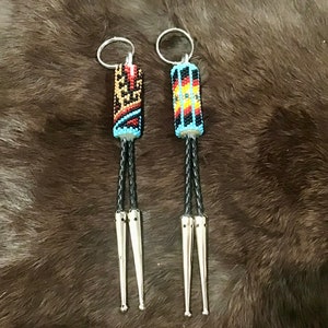 May include: Two beaded bolo ties with silver tips and black leather cords. The beads are in a geometric pattern with red, yellow, blue, black, and white colors.