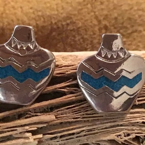 Puede incluir: Un par de pendientes de plata con una incrustación de turquesa en forma de diseño de cerámica nativa americana.