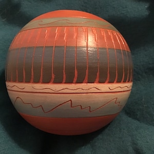 Pode incluir: Uma tigela redonda de cerâmica pintada à mão com um desenho geométrico em tons de marrom, azul e branco. A tigela tem uma superfície lisa e texturizada.