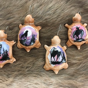 May include: Four hand-painted ceramic turtle ornaments with different designs. Each turtle features a silhouette of a wolf, a butterfly, a horse, and a bird on a purple and pink background.