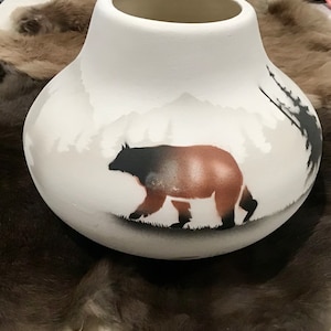 Peut inclure: Vase en céramique blanche avec une silhouette d'ours brun marchant dans un paysage de montagne. L'ours est peint avec de la peinture brune, noire et blanche.