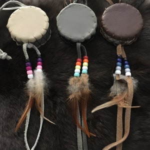 May include: Three small leather drums with feathers and colorful beads. The drums are beige, gray, and brown.