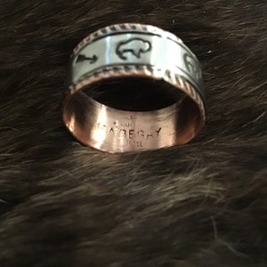 May include: A copper and silver ring with a buffalo design and the inscription "Abegay" on the inside.