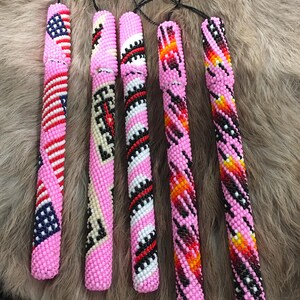 May include: Six beaded pen holders in various designs. The pen holders are primarily pink, with patterns in red, white, black, and blue. One features an American flag design. Each has a black cord attached.