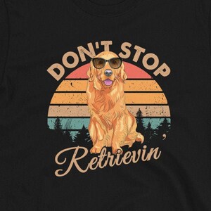 Puede incluir: Camiseta negra con un gráfico de puesta de sol retro y un golden retriever con gafas de sol. El texto "Don't Stop Retrievin'" está impreso debajo del gráfico.