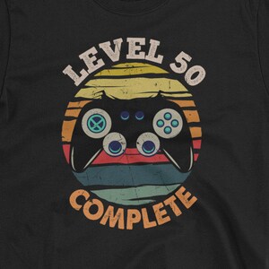 May include: Black t-shirt with a retro-style graphic of a video game controller and the text "Level 50 Complete".