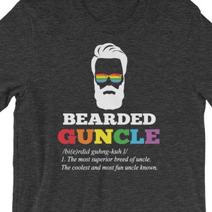 May include: A dark gray t-shirt with a white graphic of a bearded man wearing rainbow sunglasses. The text "BEARDED GUNCLE" is written in rainbow letters below the graphic. The definition of "GUNCLE" is written in white text below the graphic.