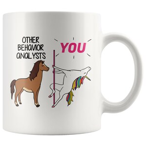 Könnte beinhalten: Weiße Keramik-Kaffeetasse mit einer humorvollen Illustration eines Einhorns, das einen Stangentanz macht, und einem Pferd, das daneben steht. Der Text lautet "Andere Verhaltensanalysten" und "Du".