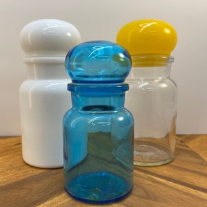 Könnte beinhalten: Drei Glasbehälter mit unterschiedlich farbigen Deckeln. Der Behälter links hat einen weißen Deckel, der mittlere Behälter einen blauen Deckel und der Behälter rechts einen gelben Deckel.