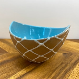 May include: A light blue ceramic bowl with a brown and white diamond pattern. The bowl is shaped like a crescent moon.