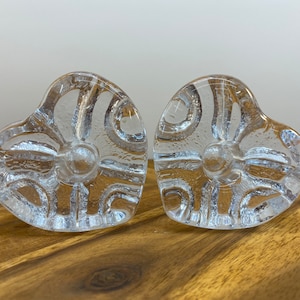 May include: Two clear glass heart-shaped candle holders with a textured swirl design.