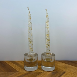 Puede incluir: Dos candelabros de vidrio transparente con destellos dorados. Los candelabros son cilíndricos y tienen una base ancha. Las velas son transparentes y tienen un diseño de destellos dorados.