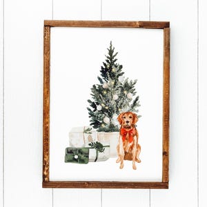 May include: A framed watercolor painting of a golden retriever dog sitting in front of a Christmas tree with presents. The dog is wearing a red bow.