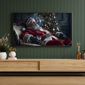 May include: A wood entertainment center with a black metal base. The center has two drawers and a shelf. A framed image of Santa Claus relaxing on a couch with a glass of whiskey and a cigar is hanging on the wall above the entertainment center. There are two vases with flowers on the shelf.