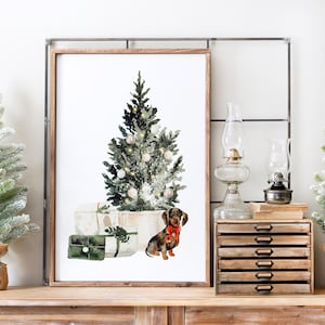 May include: A watercolor painting of a Christmas tree with presents and a dachshund wearing a red bow. The tree is decorated with white ornaments and lights. The painting is framed in a wooden frame.