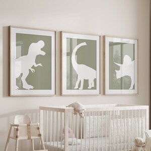 May include: A white crib with a white mattress and a white high chair in a nursery with three framed prints of dinosaur silhouettes on a light green background.