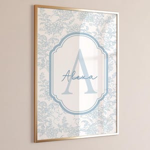 May include: A framed wall art print featuring a light blue floral pattern on a white background. Centered is a decorative light blue frame containing a large capital letter A and the name Alexa written in a cursive script font in blue.