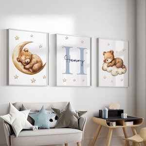 May include: Three framed prints with a nursery theme. The prints feature a sleeping bear on a crescent moon, a bear sleeping on a cloud, and the letter H with the name Henry. The prints are in a white frame with a white mat.