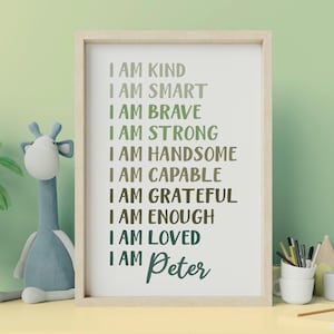 May include: A framed wall art print featuring a list of positive affirmations in shades of green, including the text I AM KIND, I AM SMART, I AM BRAVE, I AM STRONG, I AM HANDSOME, I AM CAPABLE, I AM GRATEFUL, I AM ENOUGH, I AM LOVED, and I AM Peter.