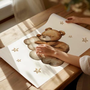 May include: A brown teddy bear sleeping on a white cloud with stars around it. The bear is holding its paws together and has its eyes closed. The cloud has a heart shape on it.
