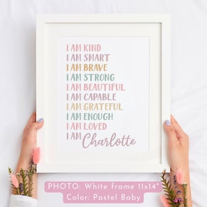 May include: A white framed print with pastel colored text that reads "I am kind, I am smart, I am brave, I am strong, I am beautiful, I am capable, I am grateful, I am enough, I am loved, I am Charlotte". The frame is 11x14 inches and the print is in pastel colors.