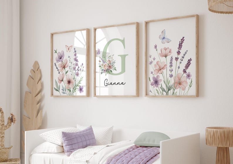 May include: Three framed floral art prints. Each print features watercolor flowers in shades of pink, purple, and lavender, with a butterfly. One print has the letter "G" and the name "Gianna". The frames are light brown.