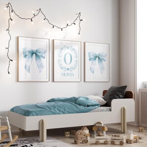 May include: Three framed prints with a blue watercolor bow design. The center print features the letter "O" in a decorative frame with the name "Olivia" below.