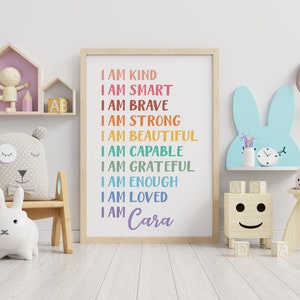 Op de afbeelding: Een kleurrijke poster met de tekst "Ik ben aardig, ik ben slim, ik ben dapper, ik ben sterk, ik ben mooi, ik ben bekwaam, ik ben dankbaar, ik ben genoeg, ik ben geliefd, ik ben Cara" in een regenboogkleurenschema. De poster hangt aan een witte muur in een kinderkamer.