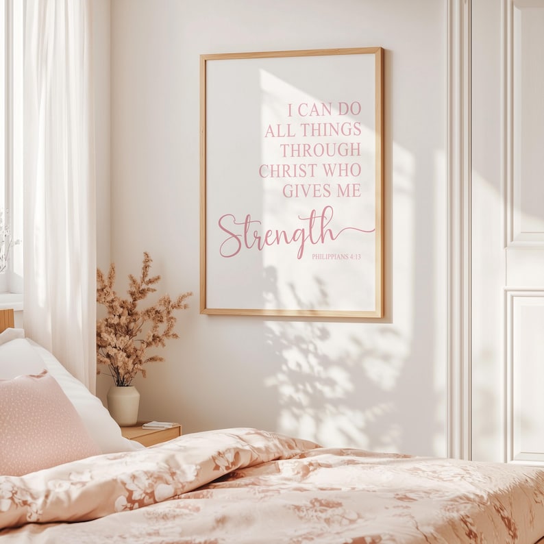 May include: A framed print with the words "I CAN DO ALL THINGS THROUGH CHRIST WHO GIVES ME STRENGTH" in pink script. The print is in a light wood frame and hangs above a bed with floral bedding.