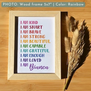May include: A framed print with a rainbow-colored text that reads "I am kind, I am smart, I am brave, I am strong, I am beautiful, I am capable, I am grateful, I am enough, I am loved, I am Bianca". The frame is made of wood and is 5x7 inches.