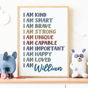 May include: A framed wall art print featuring the text I AM KIND, I AM SMART, I AM BRAVE, I AM STRONG, I AM UNIQUE, I AM CAPABLE, I AM IMPORTANT, I AM HAPPY, I AM LOVED, and I AM Willian in various colors, set in a light wood frame on a surface.