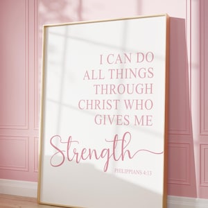 May include: A framed print with a gold border, featuring the text "I CAN DO ALL THINGS THROUGH CHRIST WHO GIVES ME Strength" in pink script. The print is leaning against a pink wall with a wooden floor.