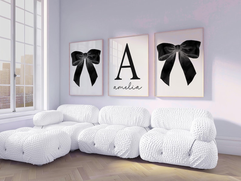 Peut inclure: Trois impressions encadr&eacute;es avec un motif de n&oelig;ud noir et une grande lettre "A" avec le nom "amelia" en &eacute;criture cursive. Les impressions sont au-dessus d'un canap&eacute; sectionnel blanc textur&eacute; dans une pi&egrave;ce lumineuse.